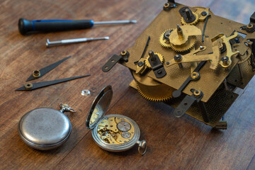 The mechanism of an antique wall clock with gears and hands. An old pocket watch on the table.