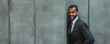 © Coosh448 - Smiling young african male in suit leaning against concrete wall