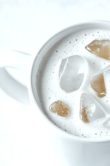 Poster - White ceramic cup filled with creamy drink and ice cubes, top view close-up on bright background. Minimalist beverage photography for menu and cafe promotion.