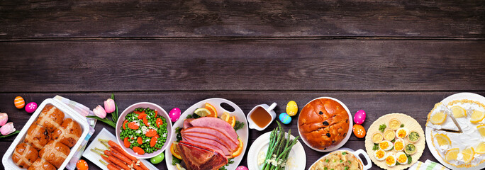 Aufkleber - Traditional Easter ham dinner. Top down view bottom border on a dark wood banner background with copy space. Ham, scalloped potatoes, vegetable side dishes, eggs, breads and lemon cake dessert.