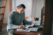 © Anna - A sad man in a warm sweater is sitting at a table with utility bills in his hands.  A dejected man calculates the increased costs of heating, gas and electricity using a calculator