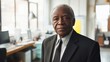 © Daiki - A portrait of an elderly Black man dressed in a suit, exuding confidence and professionalism. He stands in an office environment, showcasing wisdom and experience.