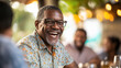 © Oppilamani - Caribbean Man in His 40s Laughing While Sitting at a Table with Friends, Enjoying a Friendly Conversation