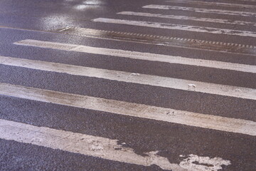 Wall Mural - A wet crosswalk on a dark street with city lights in the background.