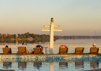 Passengers relaxing on deck chairs by a pool aboard a cruise ship on the Nile near Qena, Egypt, enjoying the sunset