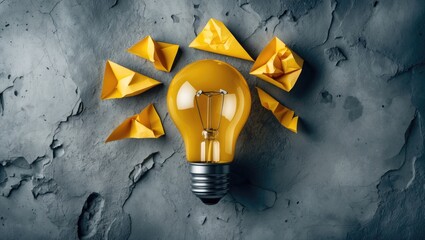 Poster - Innovative ideas and inspiration concept featuring a yellow light bulb surrounded by crumpled paper shapes on a concrete background.