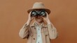© Wan_photo - A young child wearing a straw hat holds binoculars up to their eyes against a warm orange background, evoking curiosity and adventure.