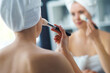 © Acronym - Young Girl is Sitting in front of a Make-up Mirror in the Bathroom and Applying a Skin Cream. Beautiful Woman is Making Cosmetic Rejuvenation Procedures.