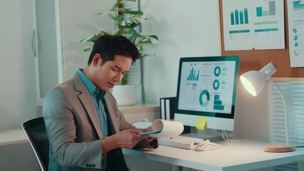 Poster - Professional businessman analyzing financial data, comparing tablet and printed documents while seated at desk in modern, well-lit corporate workspace during evening hours
