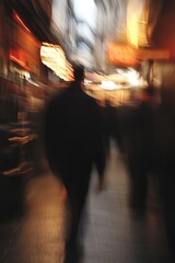 Poster - Blurry City Street Scene with Silhouette of a Person Walking Through a Vibrant Alley at Night : Generative AI