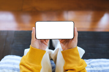 Wall Mural - mockup image of a woman holding mobile phone with blank desktop screen while sitting on the bed at h