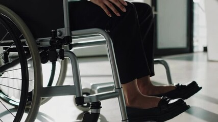Poster - Businesswoman sitting in a wheelchair and touching her knee, captured in a slow motion sequence, emphasizing vulnerability and resilience in the workplace