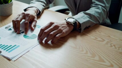 Fototapete - Businessman wearing a smartwatch examines financial documents with charts and graphs, meticulously analyzing data in a slow motion sequence