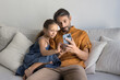 © fizkes - Mature Portuguese man his little daughter resting on couch using smartphone, messaging, videocalling, exploring new AI mobile application, play videogame or buying services via marketplace platform