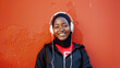 © DEIB Visuals - Candid photo of a happy african american muslim teenager listening to music. Smiling black woman wearing a hijab and white headphones. Copy space for text. Positivity & happiness. Red wall background