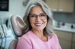 © Nasima - A middle-aged woman with gray hair and glasses smiles while sitting in the dentist's chair, wearing pink