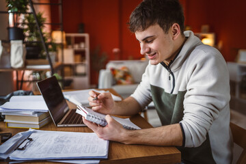 Wall Mural - young man student study for exam notebook, laptop and clipboard at home