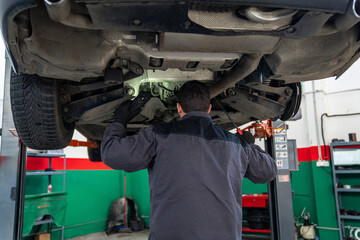 Poster - Serviceman checks car suspension on a column lift in car service.