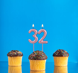 Wall Mural - Three birthday cupcakes with number 32 candle - Blue background.