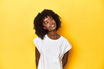 Teen girl in white tank top, yellow studio background relaxed and happy laughing, neck stretched showing teeth.