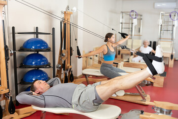 Wall Mural - Adult man in sportswear training her legs with straps in pilates studio..