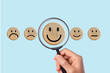 © Foto Art - Hand holding magnifying glass focusing on happy face wooden block among various emotions, customer satisfaction, and positive feedback concept