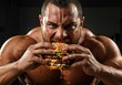 © IbragimovN - Muscular man intensely eating a large juicy burger under dramatic lighting