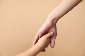 Wall Mural - Mother and child holding hands on beige background, closeup