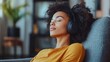 © Pat J. - A calm young woman in casual attire, seated on a grey armchair in a sleek living room, listening to music through headphones with closed eyes, showcasing relaxation