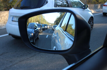 Fototapete - Heavy traffic takes up all lanes on a country road. View of a traffic jam in a car mirror with blurred vehicles on a road
