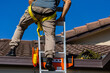 © Austockphoto - Tradie climbing on roof of house in safety harness to secure rope for safety compliance
