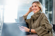 © Westend61 - Young woman in a sweater holding a cell phone and smiling indoors