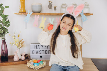 Portrait of happy little girl wearing bunny ears holding colored Easter eggs