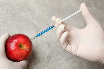 Wall Mural - GMO concept. Scientist injecting something into fresh apple at grey table, closeup