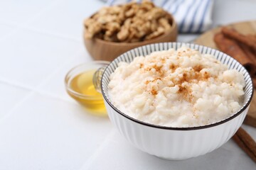 Wall Mural - Tasty rice pudding with cinnamon served on white tiled table, closeup