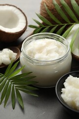 Wall Mural - Organic coconut cooking oil in jar, spoon, fresh fruits and green branches on grey table, closeup