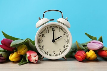 Aufkleber - Spring time. Alarm clock and beautiful tulips on wooden table against light blue background