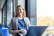 © Westend61 - Happy blond businesswoman holding laptop near window in office