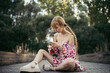 © Westend61 - Young woman wearing summer dress with floral design sitting on boardwalk looking at cell phone