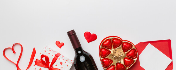 Wall Mural - Bottle of red wine on colored background for Valentine Day with gift box, envelope and chocolate. Heart shaped with gift box of chocolates top view with copy space