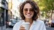 © Z A C - Smiling woman holding coffee cup outdoors.