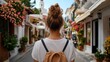 © iuricazac - A woman with brown hair wearing a backpack stands in the center of a European street lined with shops and buildings, looking towards the viewer.
