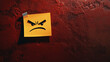 © PhotoArtHub - A yellow sticky note with an angry face drawn on it is attached to a textured red wall, symbolizing frustration or negative emotions in a visual and expressive manner.