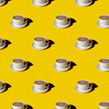 White cup of cappuccino coffee with plate pattern on yellow background.