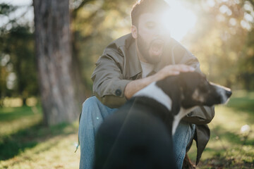 Wall Mural - A joyful moment captured as a man interacts with his dog amidst sunlit park surroundings. The sunlight filters through the trees, creating a warm and serene atmosphere.