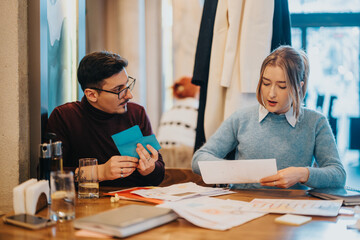 Wall Mural - Two professionals engaged in a discussion while reviewing papers together at a busy workspace table. The scene emphasizes teamwork, productivity, and focus in a modern corporate environment.