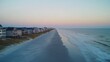 © A B I G A I L - Aerial sunset view of beach houses, ocean waves, and tranquil coastal scene; idyllic vacation backdrop