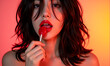 © Celt Studio - Attractive woman enjoying lollipop closeup shot sensual lips. glossy makeup beauty portrait soft lighting warm pink orange background. delicious sweet candy seduction, romantic mood