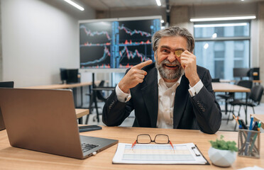 Wall Mural - Expressive senior male office worker is with crypto coin in hand before the eye, smiling