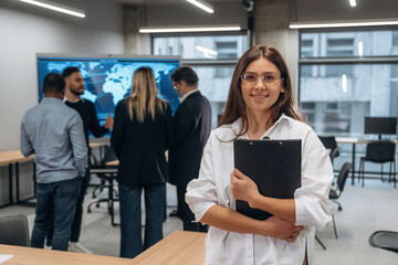 Woman is looking at the camera. Group of office workers are indoors together